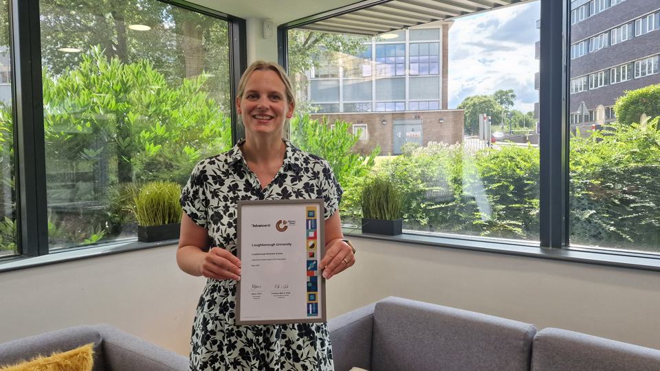 Person standing in an office setting with large windows and greenery outside, holding a framed certificate.